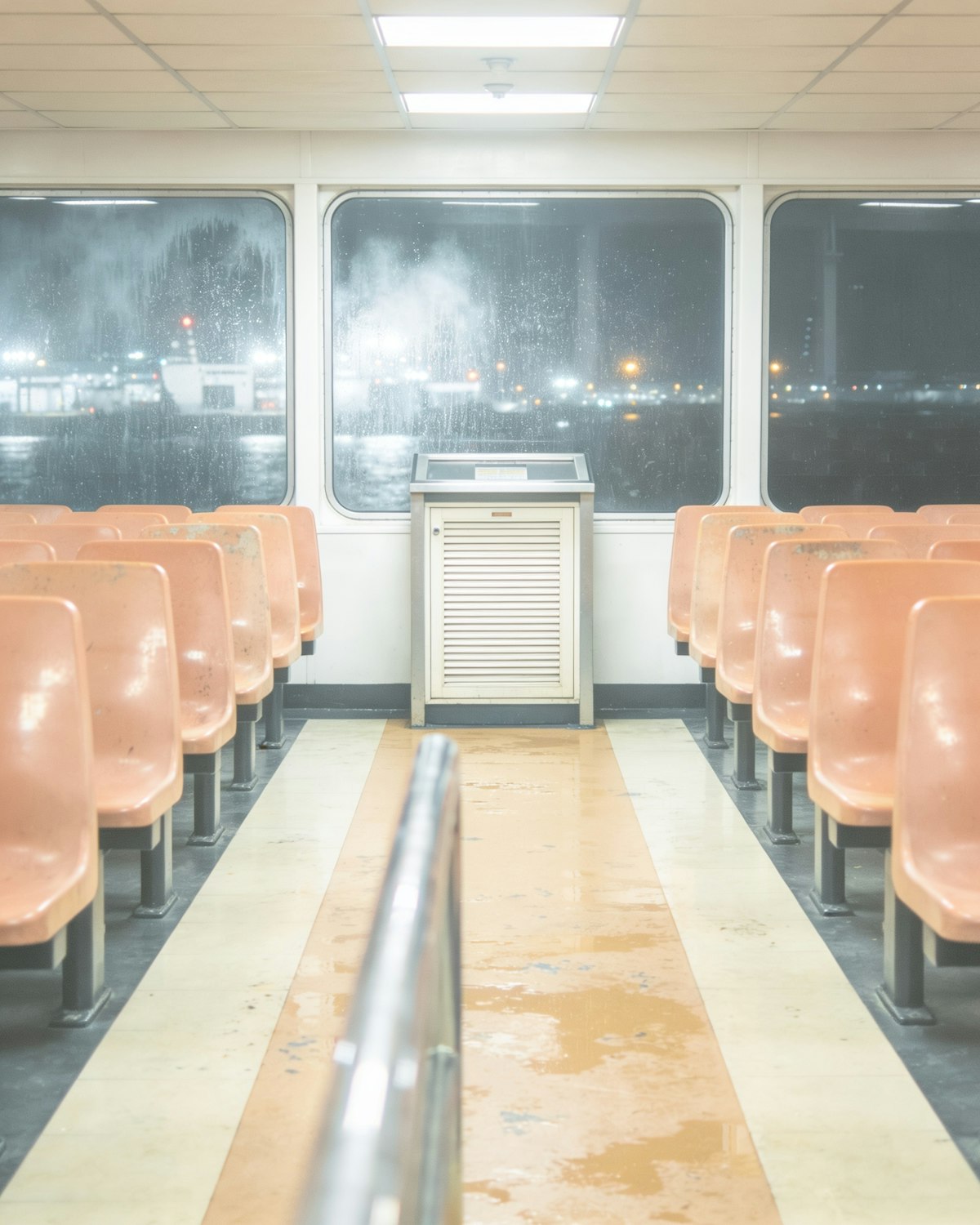 The interior of a harbour ferry at night, rows of orange bench seats facing rain-streaked windows